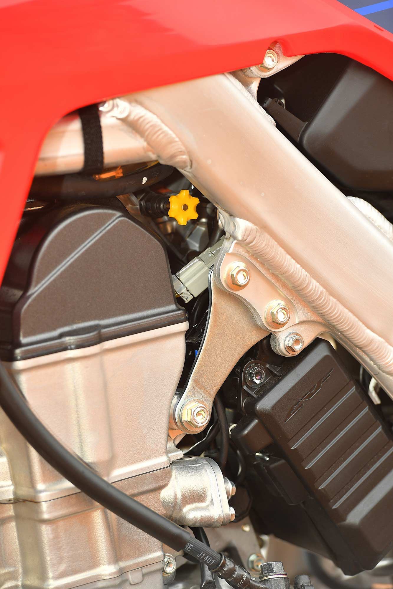 Steel engine hangers replace the previous models’ aluminum counterparts. The yellow choke knob doubles as the idle adjustment screw: Counterclockwise adjustment turns the idle up, clockwise drops the revs and lowers the idle. The battery is tucked neatly behind the black CRF logo’d plastic cover as well.