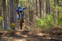 2024 Yamaha YZ250X cavalgando sobre o salto na trilha da floresta